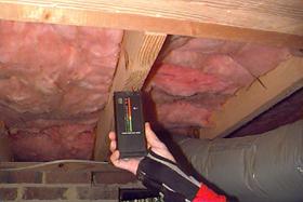 A moisture meter pressed into a floor joist.